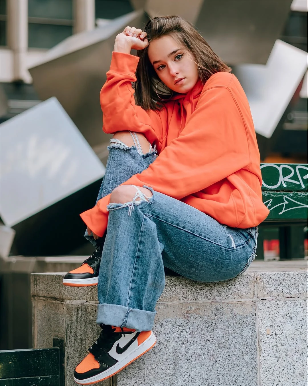 Retrato en exterior de una joven sentada con sudadera naranja.